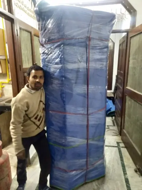 Packer standing with a wrapped wardrobe after packing
